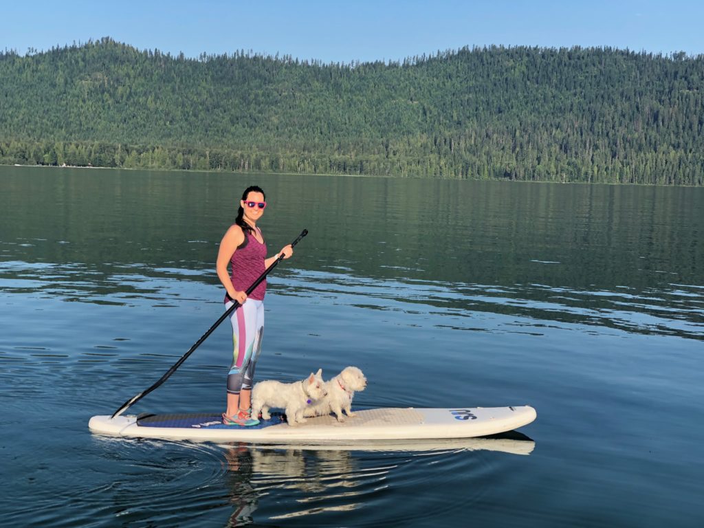 Julie K paddle boarding on lake with two white dogs