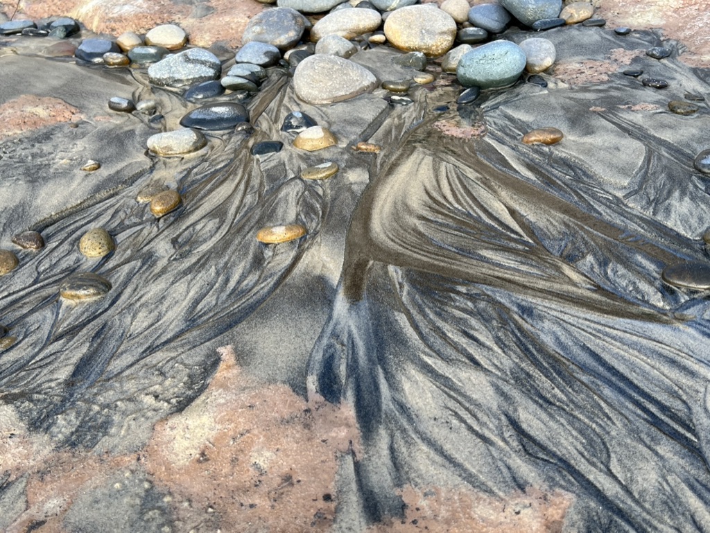 water running through sand and rocks creating riveting pattern