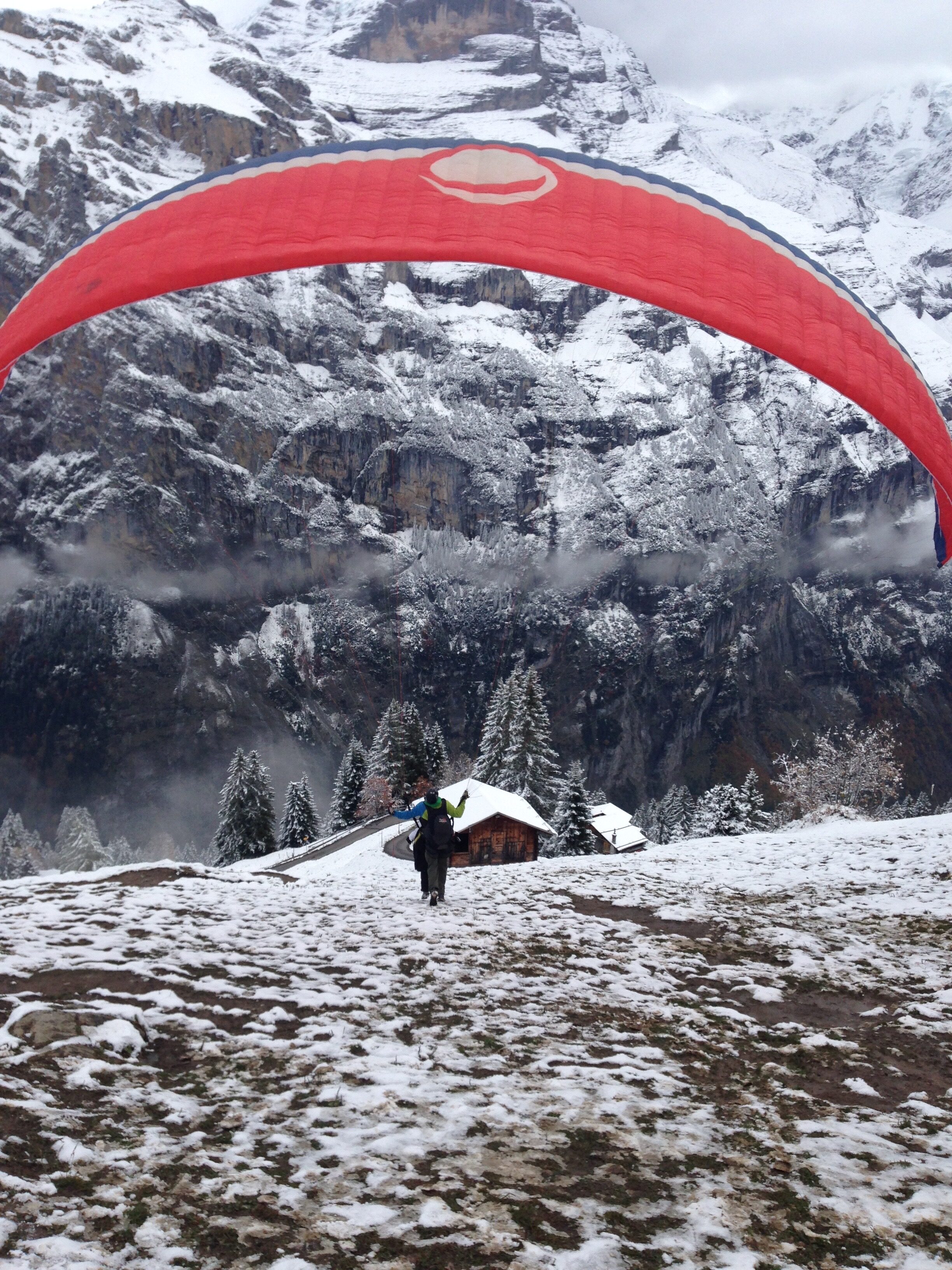 Paraglide launch with red sail and light snow in Swiss Alps
