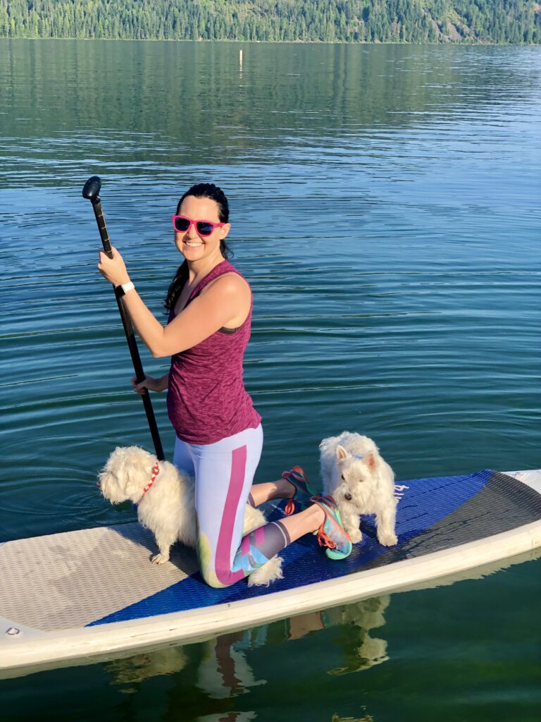 Julie K paddle boarding on the lake with 2 white dogs